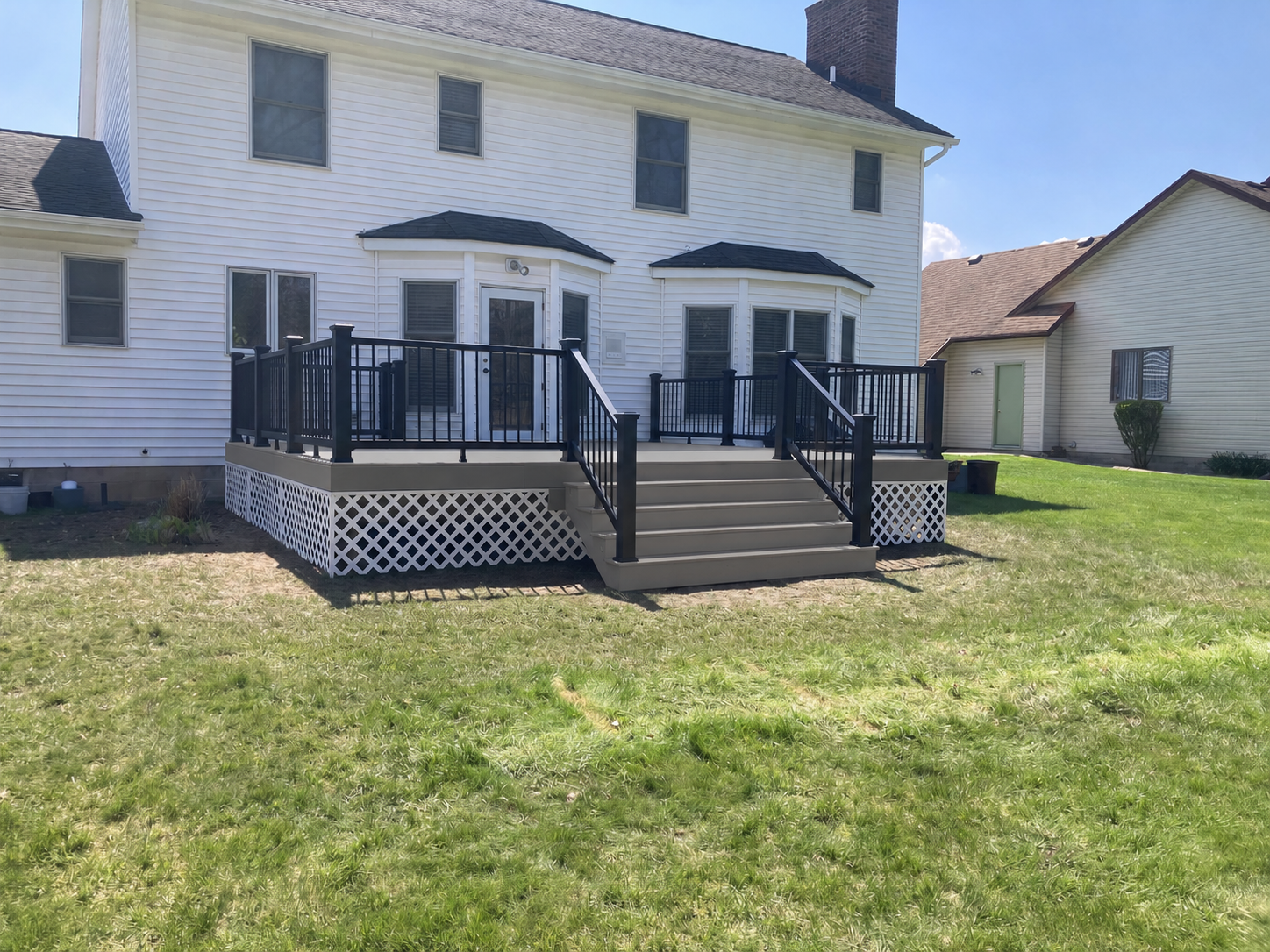 Taupe composite deck with black aluminum railing, wide center steps, and white lattice skirt