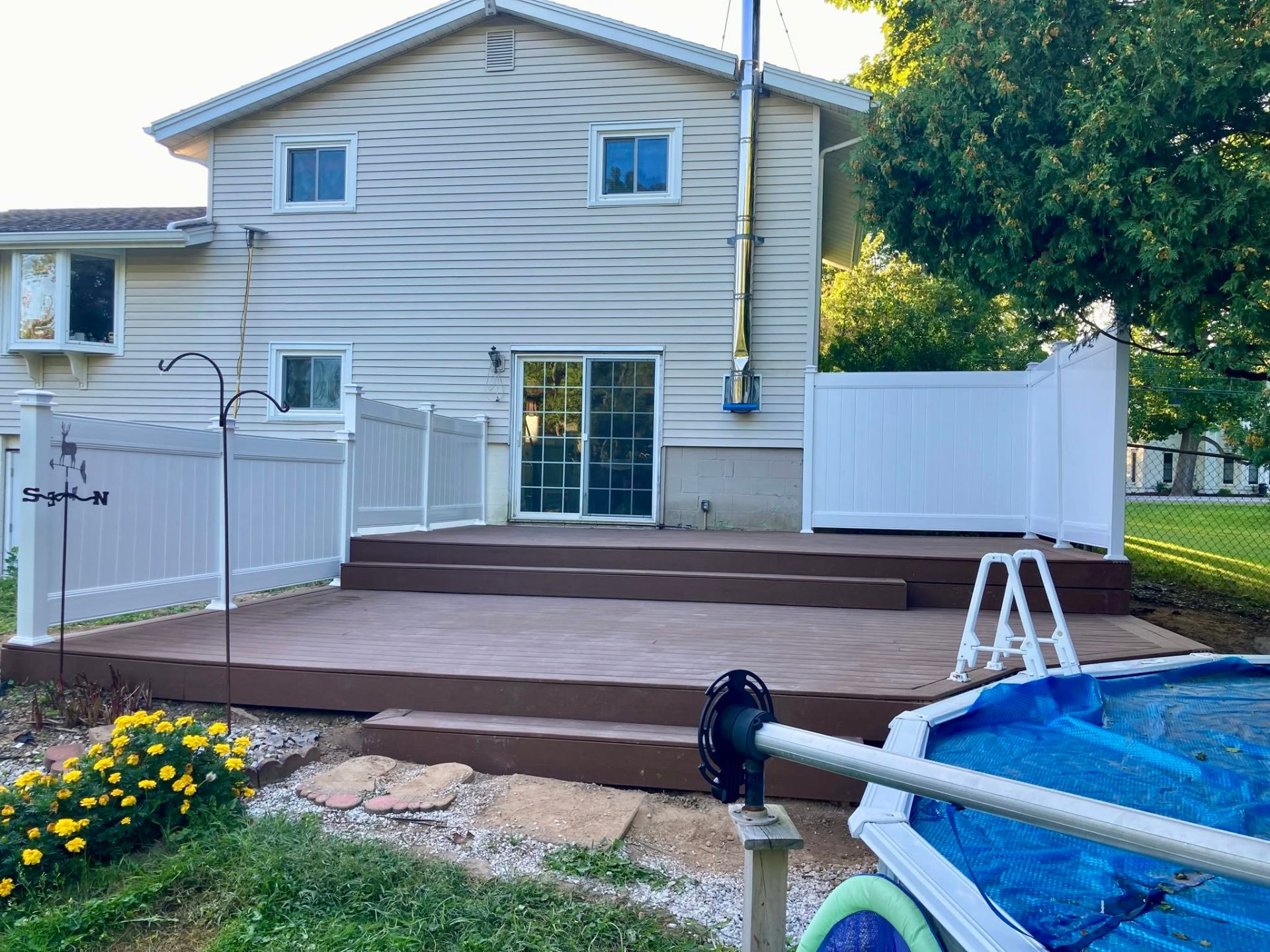 Two-tier brown composite deck with white vinyl privacy fence and wide steps