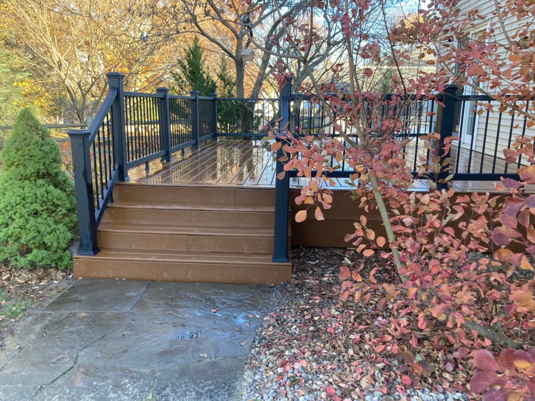 Brown composite deck with steps and black aluminum railing surrounded by fall foliage