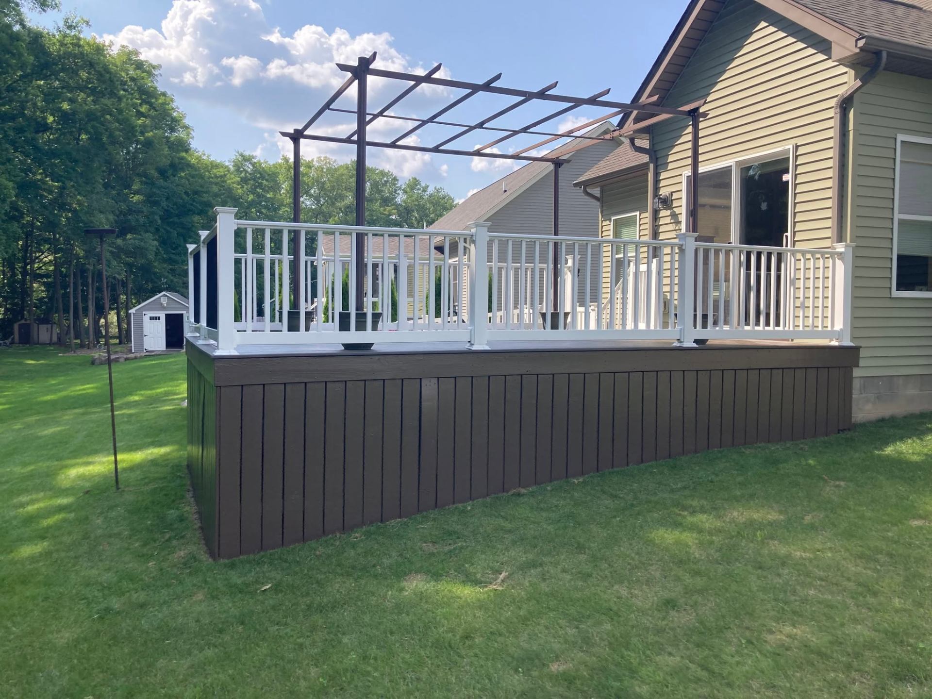 Brown composite deck with white railing and cedar pergola overhead
