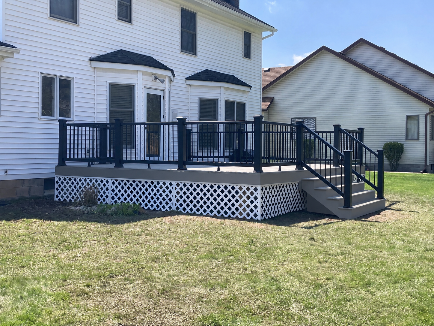 Side view of a taupe composite deck with black rail and white lattice skirt