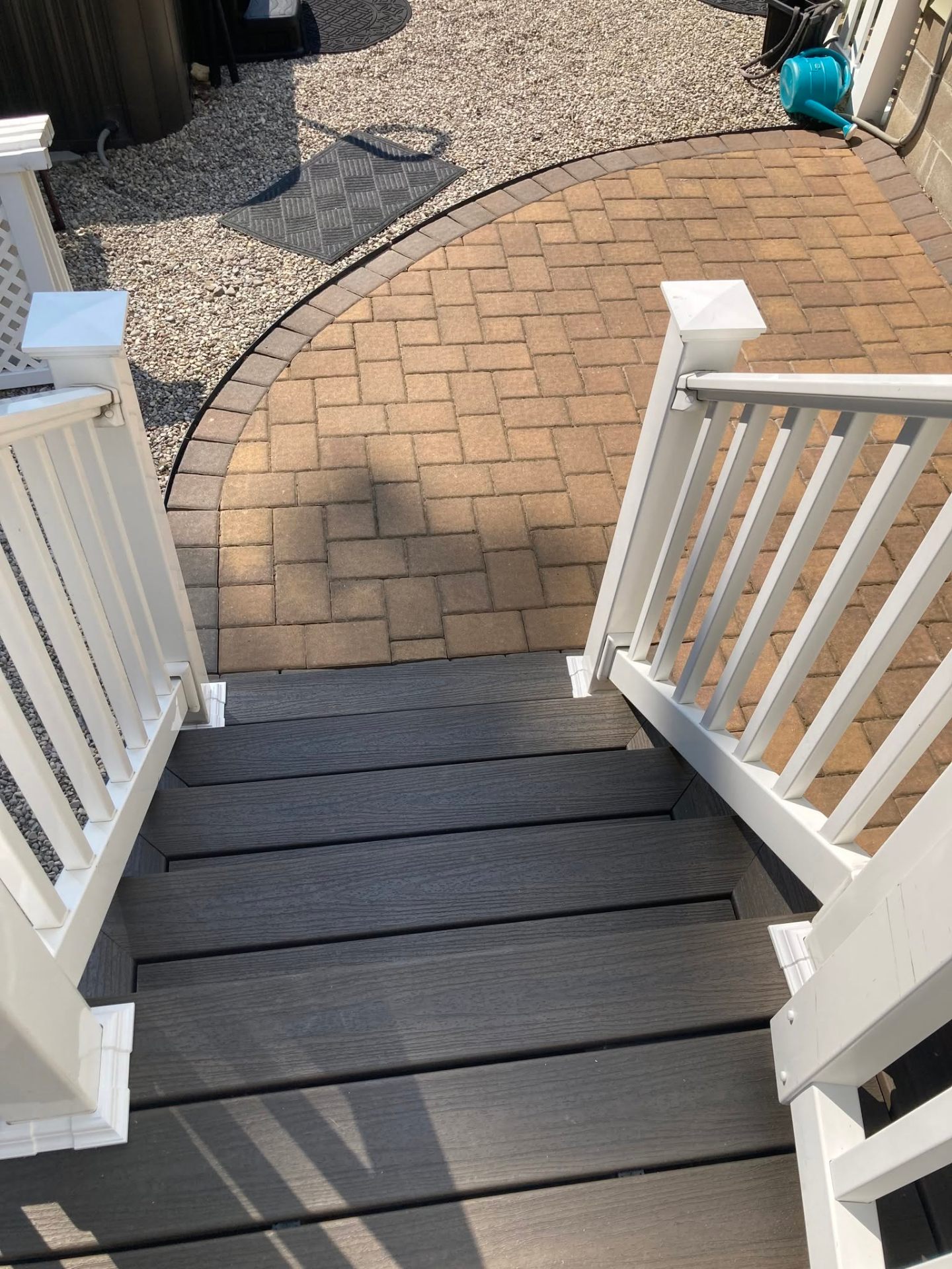 Composite stairs with white vinyl railing stepping down to a paver patio