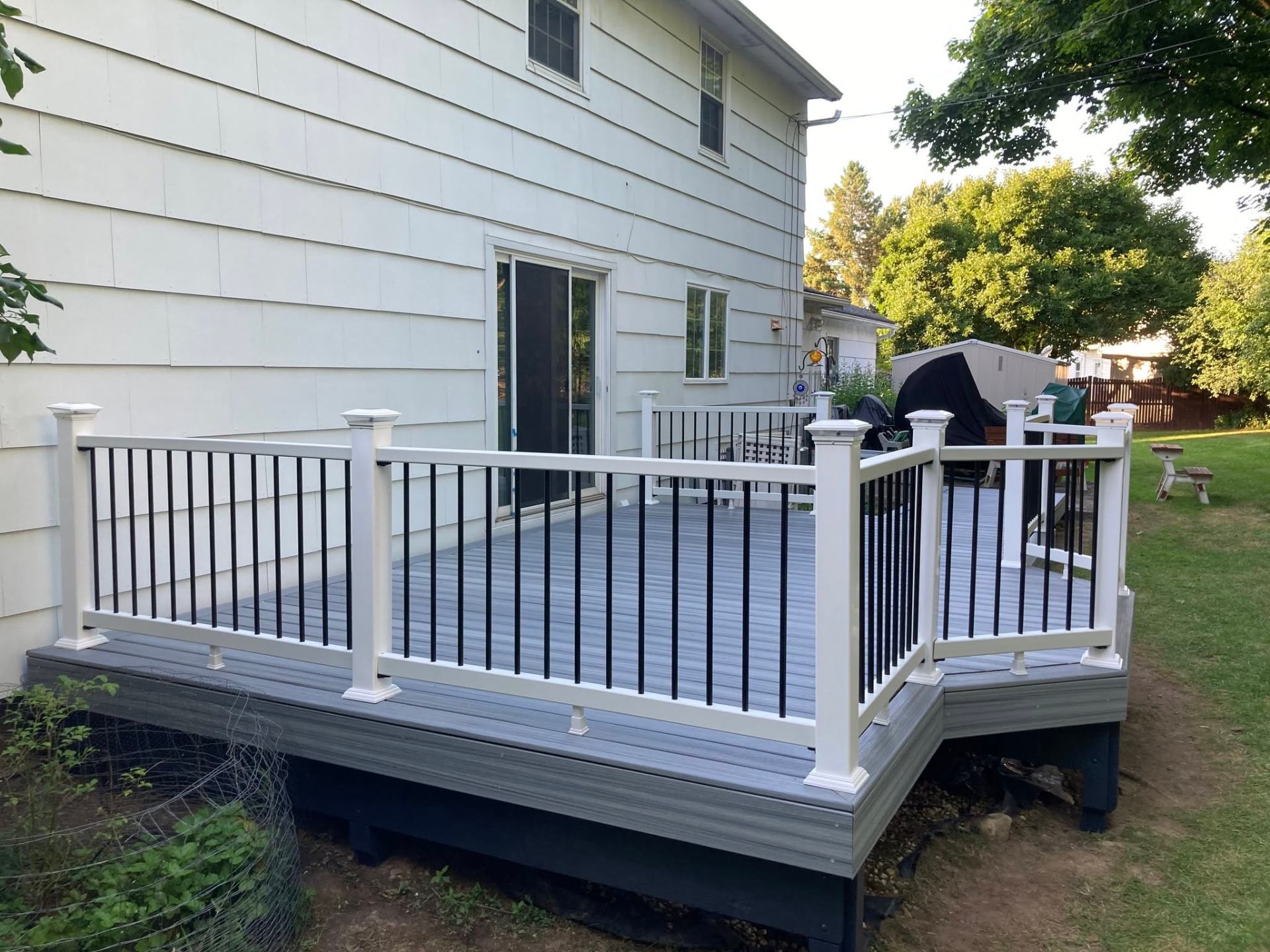 Gray composite deck wrapping the back of a home with white posts and black balusters