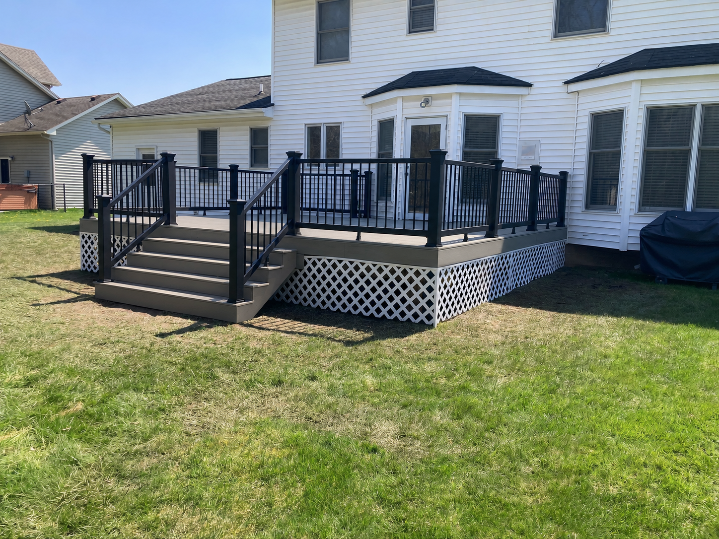 Angled view of a taupe composite deck with black railing wrapping around the back of a colonial home