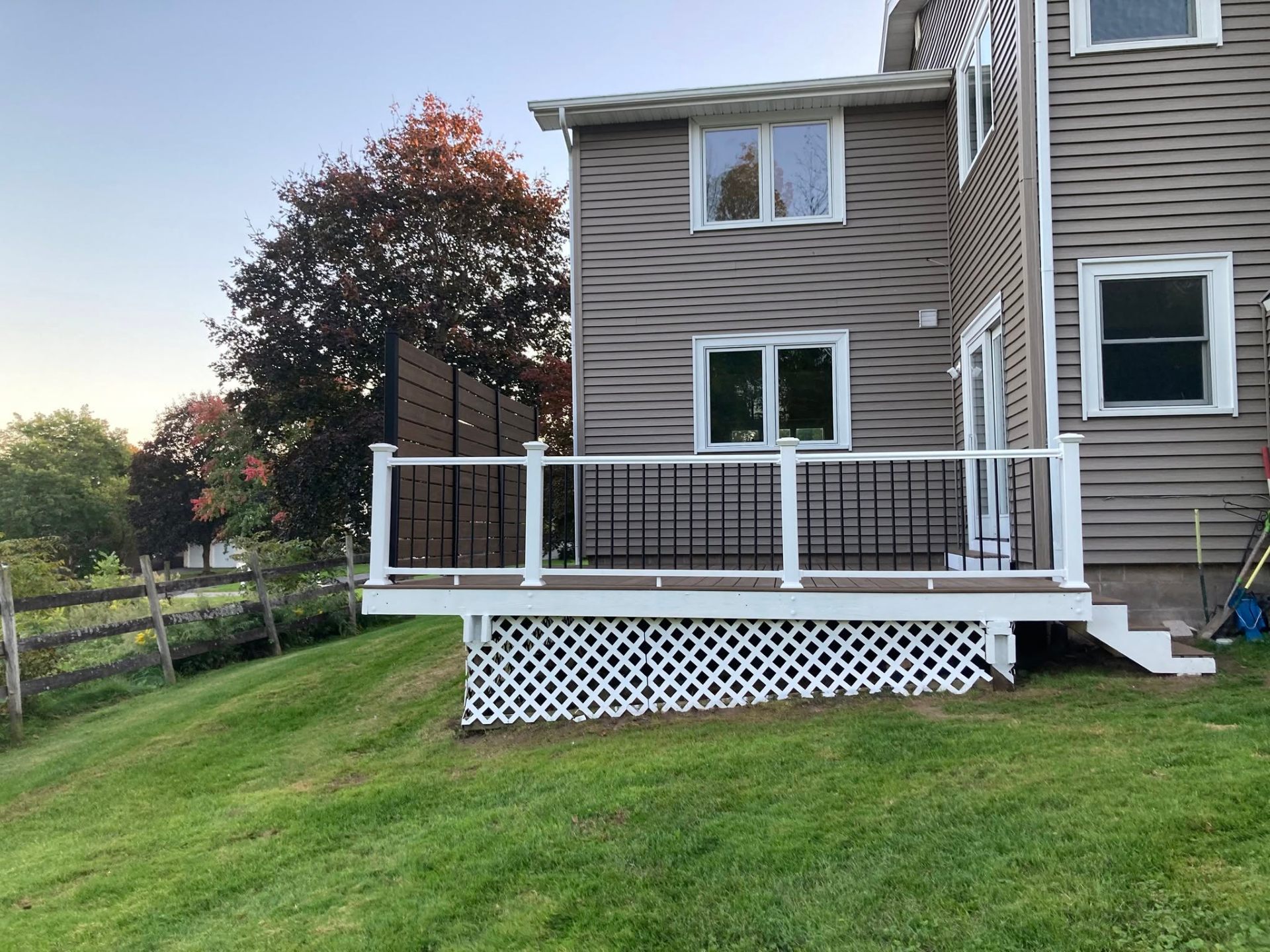 Brown composite deck with white posts, black balusters, and a horizontal privacy screen